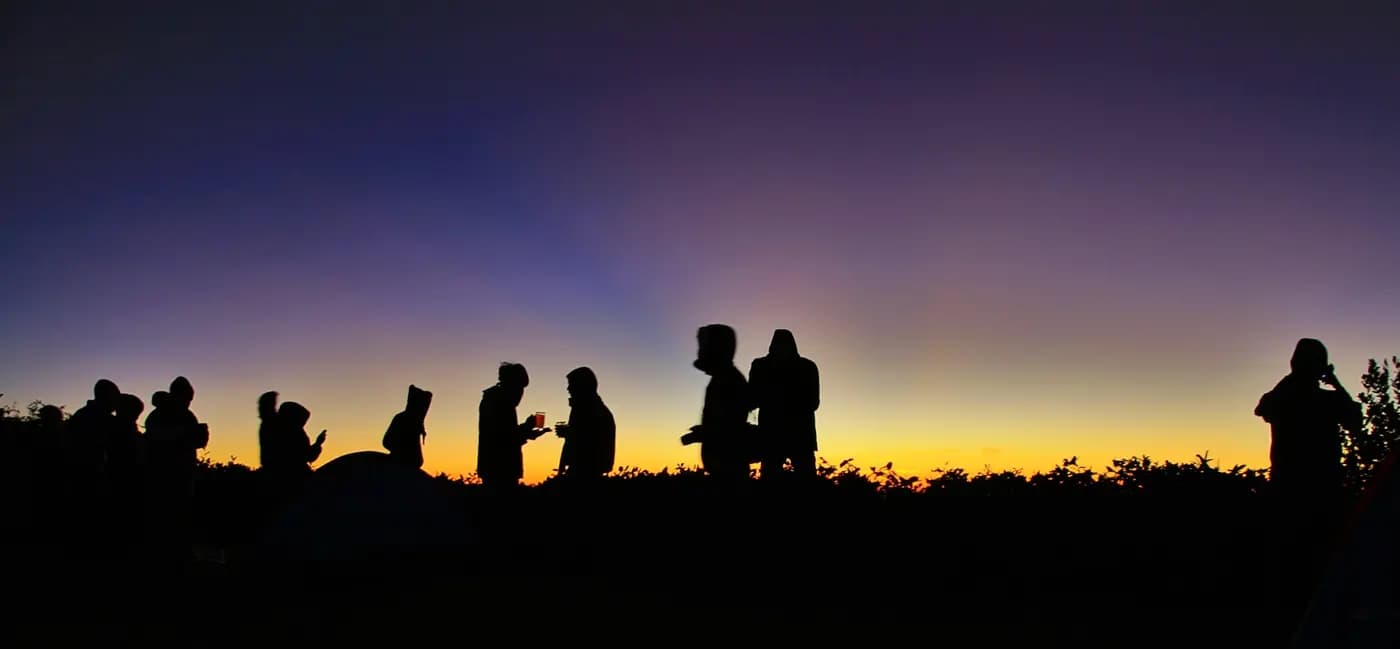 Siluet rombongan pendaki berbincang sambil memegang gelas minuman saat langit fajar di puncak Gunung Lawu