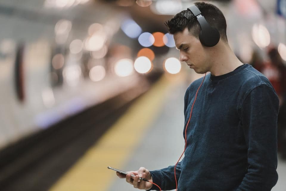 Seorang pria berheadphone melihat ponsel sambil menunggu di peron stasiun