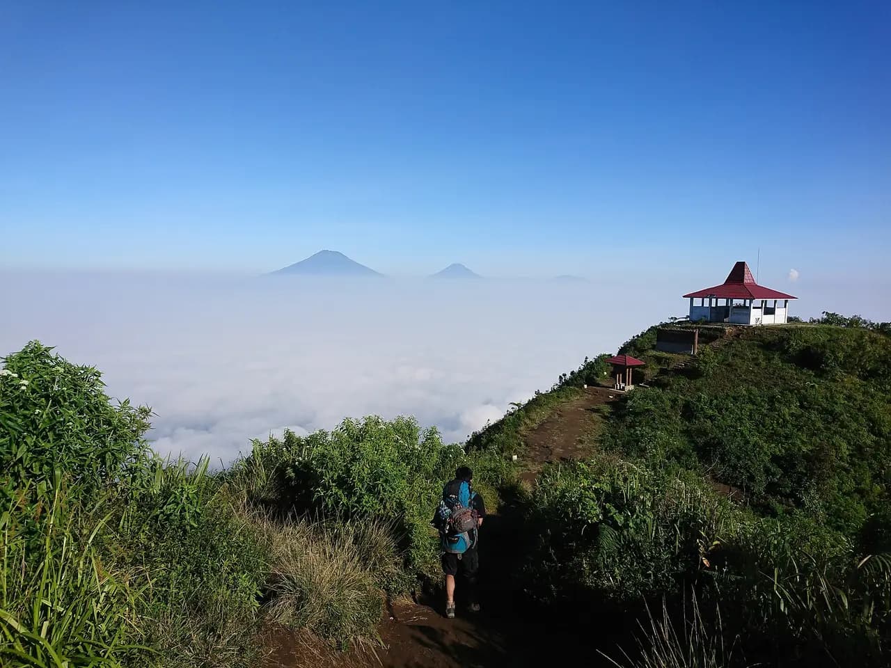 Pendaki berjalan di jalur punggungan puncak Gunung Andong menuju bangunan beratap merah