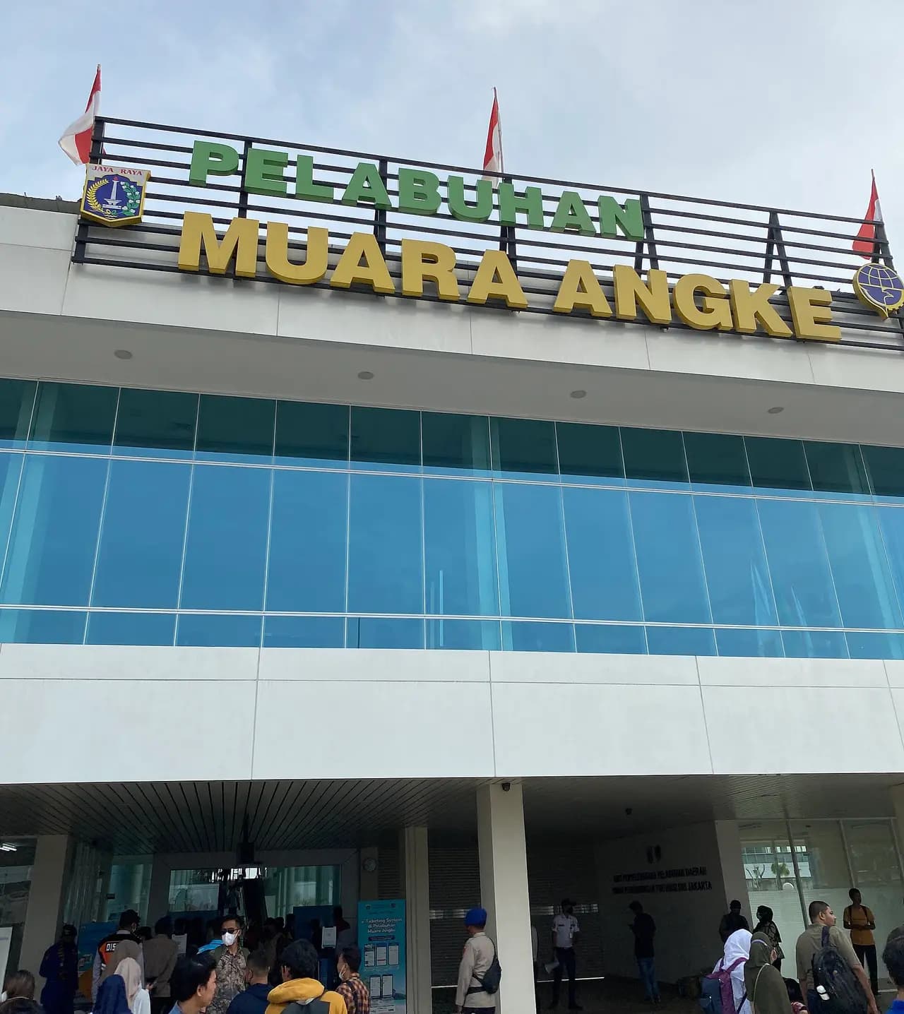 Gedung Pelabuhan Muara Angke dengan papan nama besar, calon penumpang berkumpul di depan pintu masuk