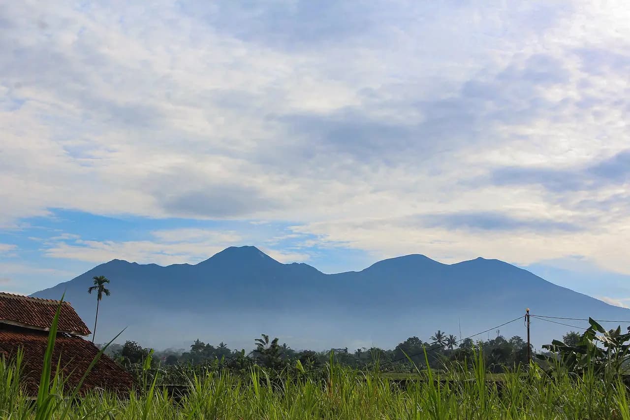 Gunung Gede dan Gunung Pangrango dilihat dari Karangtengah, Cibadak, Sukabumi, dengan sawah dan atap rumah di depan