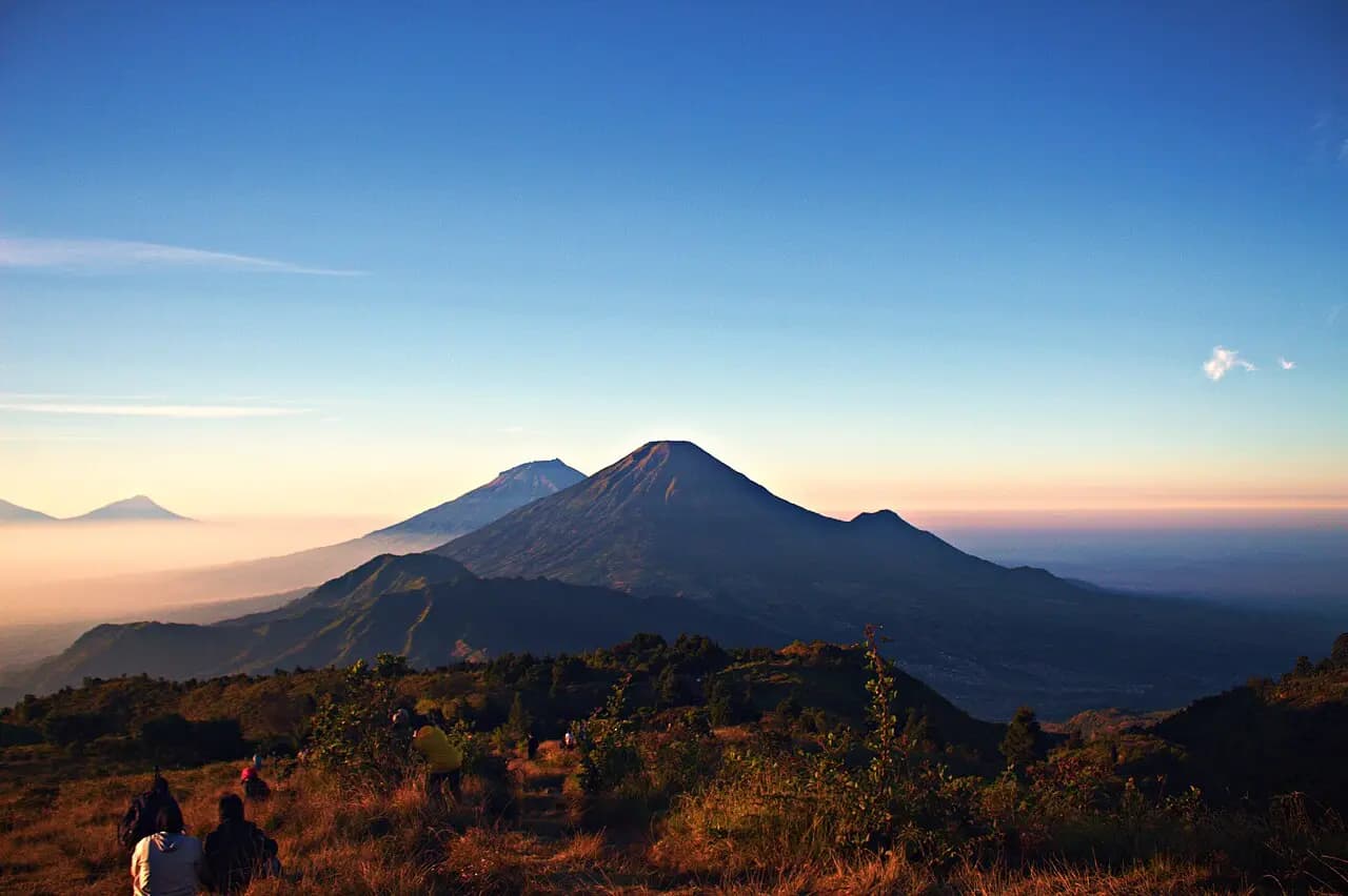 Gunung Sindoro saat matahari terbit dengan puncak kecil di sisi kanannya, Gunung Sumbing di belakang kiri, dilihat dari Gunung Prau