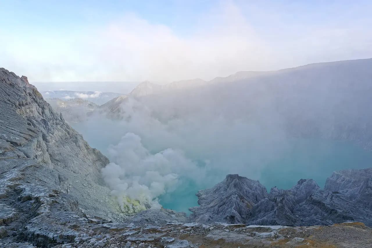 Danau kawah Ijen berwarna hijau tosca dengan asap belerang dari tepi danau, dilihat dari bibir kawah