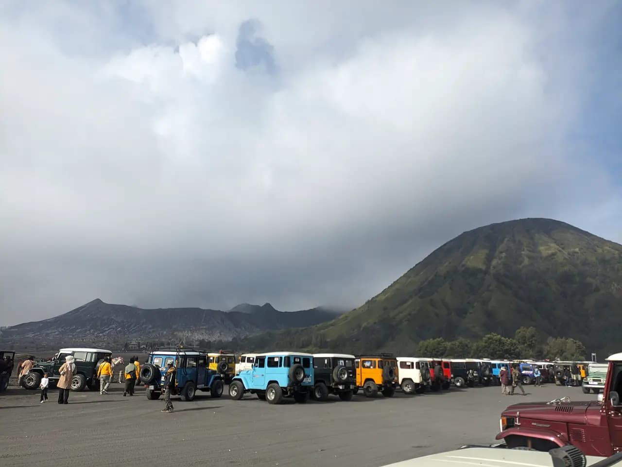 Deretan jip wisata parkir di Lautan Pasir Bromo dengan Gunung Batok di latar belakang
