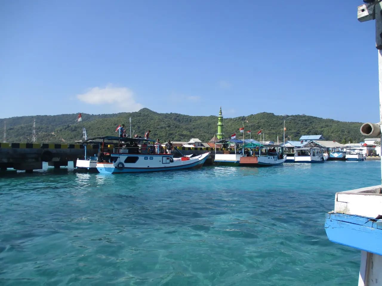 Perahu-perahu kayu bersandar di dermaga Pelabuhan Karimunjawa dengan bukit hijau di belakang