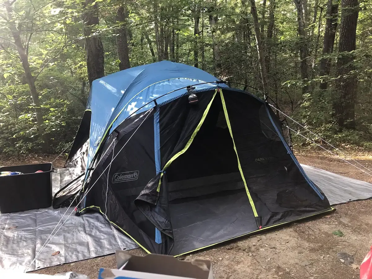 Tenda dome biru berdiri di atas alas terpal dengan tali penarik yang terpasang ke tanah di area hutan