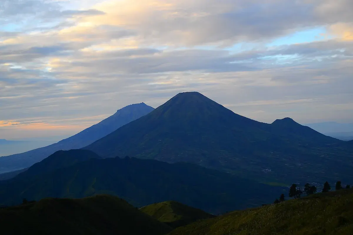 Pemandangan dari puncak Gunung Prau saat langit pagi mulai terang, dengan kerucut gunung besar di tengah