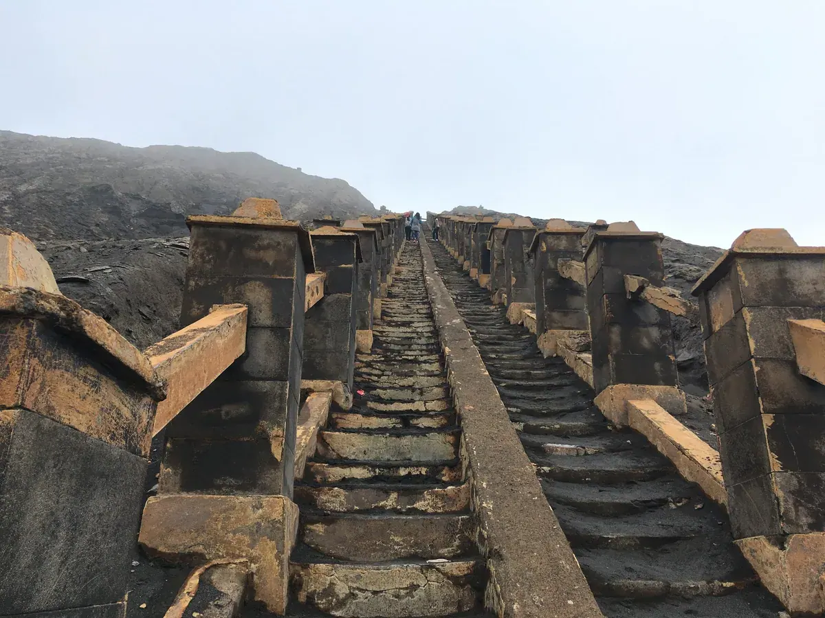 Tangga batu menuju kawah Gunung Bromo dengan beberapa pengunjung berjalan di bagian atas