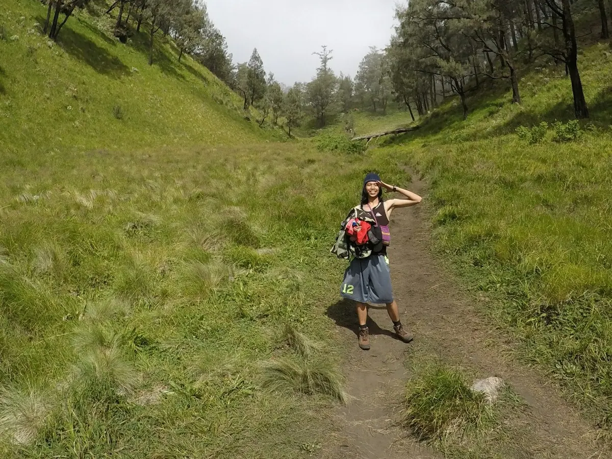 Pendaki perempuan dengan ransel kecil dan sepatu gunung berpose di jalur berumput dekat Pos 6 jalur Candi Cetho, Gunung Lawu