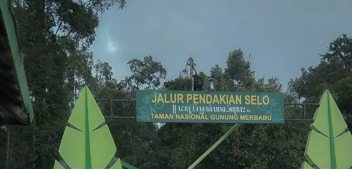 Gerbang Jalur Pendakian Selo bertuliskan Taman Nasional Gunung Merbabu, dengan papan nama hijau di antara pepohonan