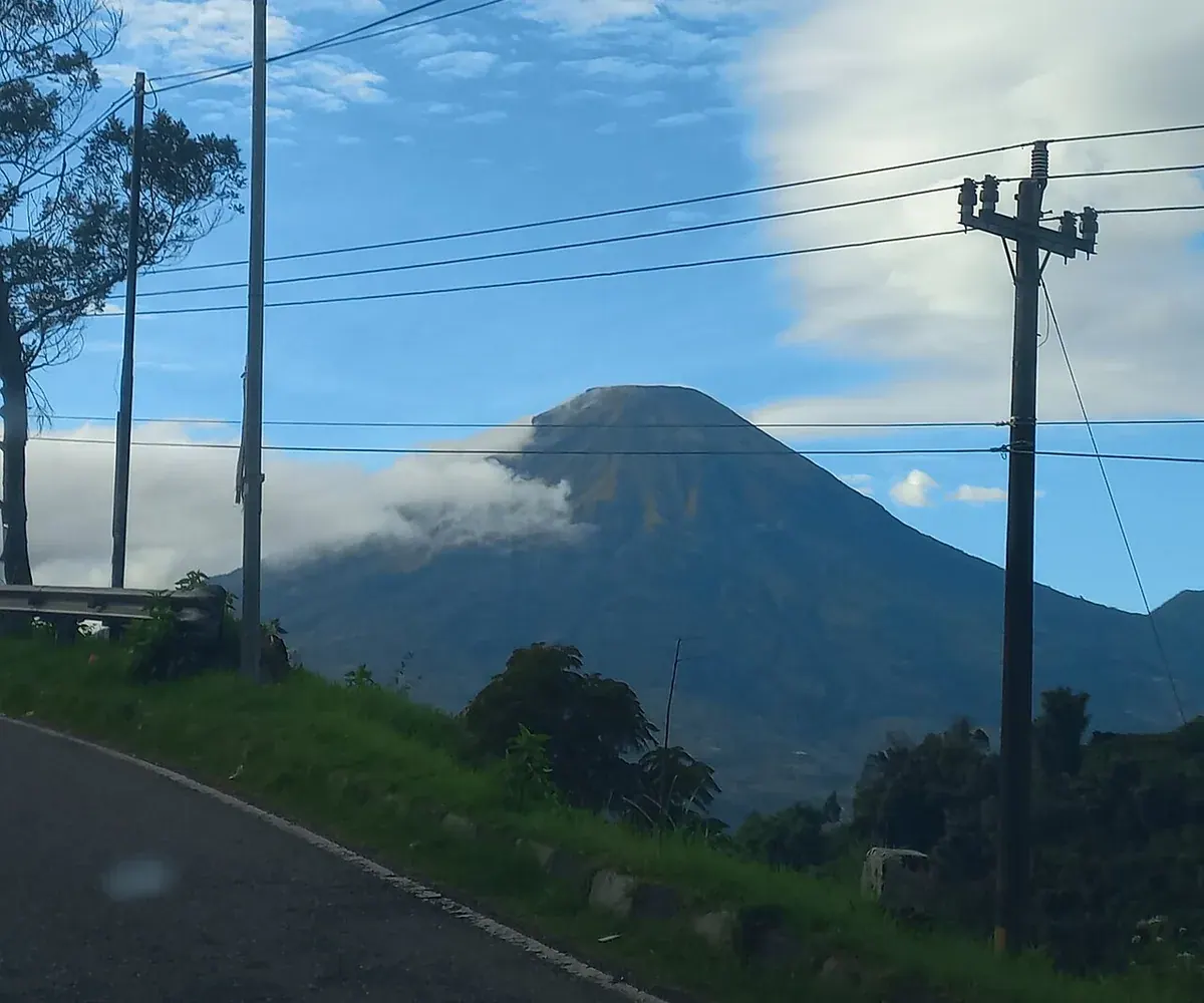 Kerucut Gunung Sindoro di bawah langit biru, dilihat dari tepi jalan dengan tiang listrik di kanan
