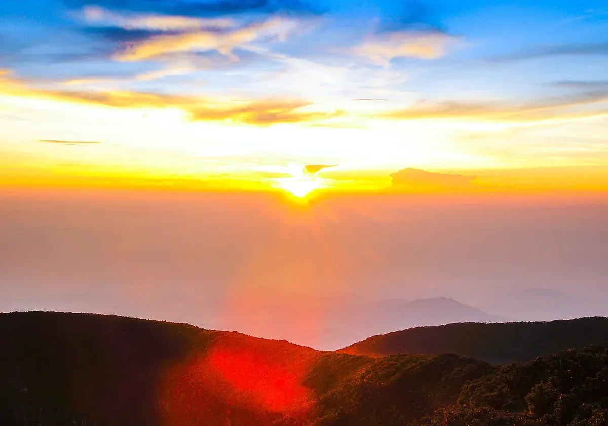 Matahari terbit di atas lapisan kabut, dilihat dari puncak Gunung Gede, dengan punggungan berhutan di latar depan