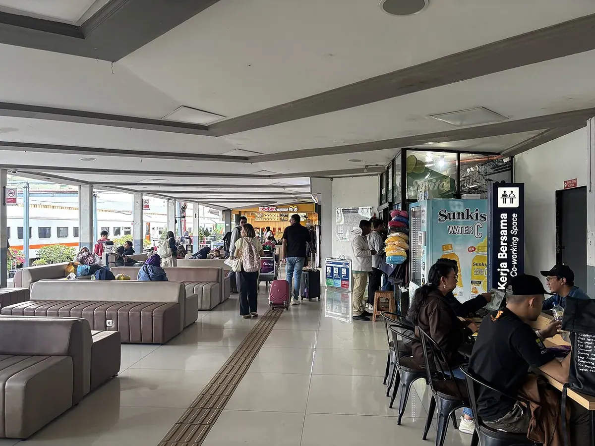 Ruang tunggu Stasiun Bandung yang ramai penumpang, dengan deretan sofa, koper, dan area kerja bersama
